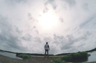 Rear view of man standing at riverbank against sky