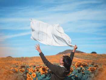 Rear view of woman with arms raised on field against sky