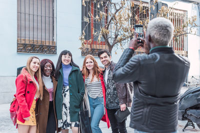 Back view of unrecognizable black male taking photo of company of multiracial friends standing on street together