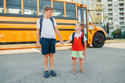  brothers students with hearing aids by yellow school bus.  kids with disabilities holding hands