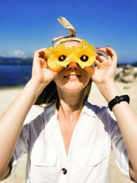 Smiling young woman holding flowers over eyes at beach