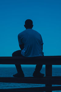 Rear view of silhouette man sitting against sea