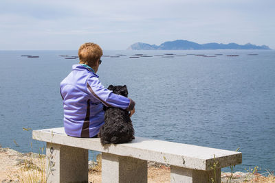 Lonely woman senior with her dog looking at the sea