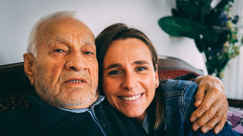 Portrait of grandfather with arm around granddaughter while sitting on sofa at home