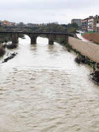 Arch bridge over river in city against sky