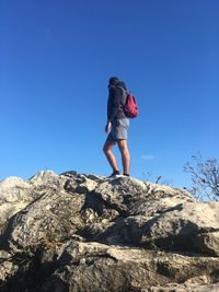 Low angle view of man standing on rock against clear blue sky