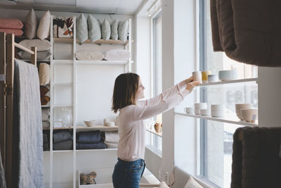 Side view of female entrepreneur arranging products on shelf in store