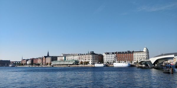 View of buildings by river against blue sky