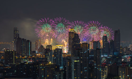 Firework display over illuminated buildings against sky at night