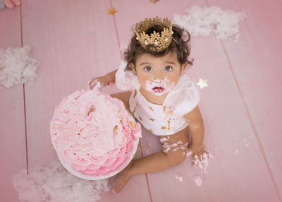 Cute baby girl with birthday cake sitting at home