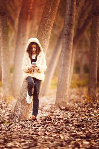 Full length of girl using phone while leaning on tree at field