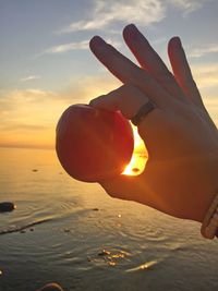 Person holding ice cream against sea during sunset