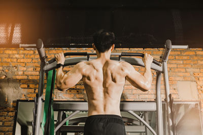 Rear view of shirtless man exercising at gym