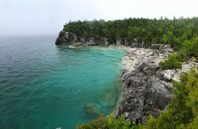 Scenic view of rocks by sea against sky