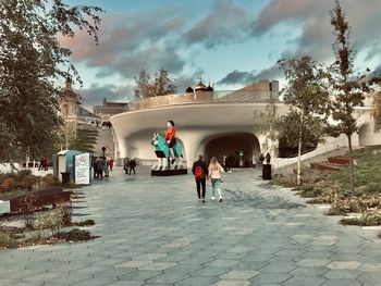 People on sidewalk in city against sky