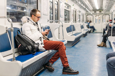 Handsome adult man in glasses riding in subway train. in hands male hold smartphone. copy space.