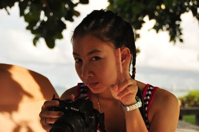 Close-up portrait of young woman holding camera gesturing