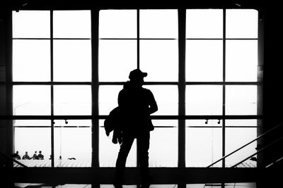 Rear view of silhouette person standing by glass window