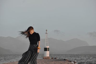 Woman standing on pier by sea against sky