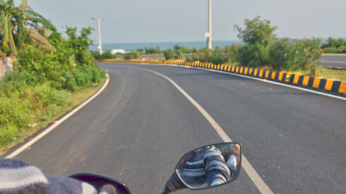 Low section of man on road by trees against sky