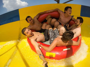 Friends sitting in inflatable ring on slide against sky