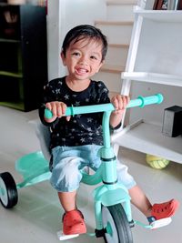 Portrait of smiling boy sitting on tricycle at home