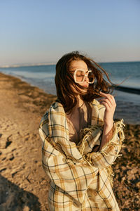 Young woman standing at beach against sky