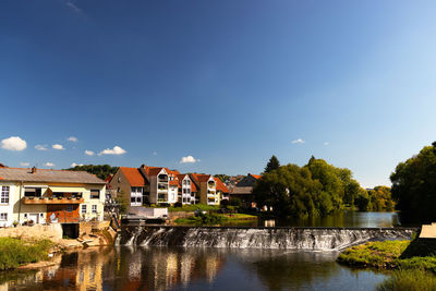 Buildings by river against blue sky