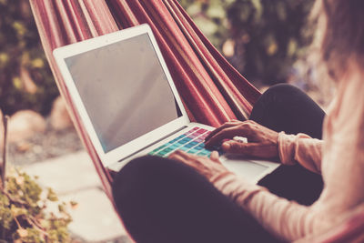 Midsection of woman using laptop while sitting on hammock