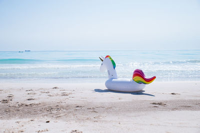 Unicorn shape inflatable ring at beach against sky