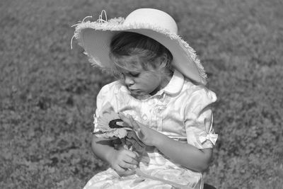 Girl wearing hat holding flower on field