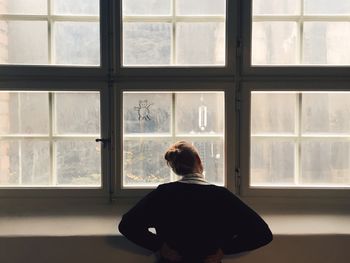 Rear view of woman with hands on hip looking through window