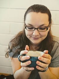 Close-up of woman holding coffee cup against wall