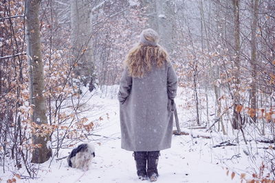 Rear view of woman standing in forest during snowfall