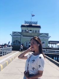 Young woman standing in city against clear sky during sunny day