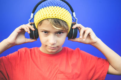 Close-up of portrait of boy listening to music while standing against blue background