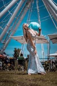 Full length of young woman holding cotton candy against ferris wheel on land