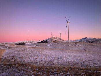 Wind turbines on land against sky during sunset