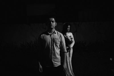 Full length of man looking away while standing against wall at night