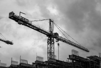 Low angle view of cranes at construction site against sky