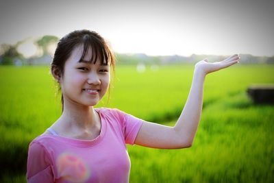 Portrait of smiling teenage girl gesturing at farm against clear sky