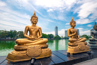 Buddha statues on retaining wall by lake against sky