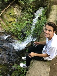 Portrait of smiling young woman sitting on rock by plants