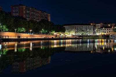 Illuminated buildings by river against sky at night