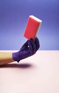 Close-up of hand holding umbrella against blue wall