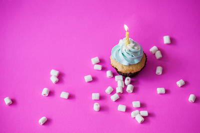 Lit candle on cupcake over pink background