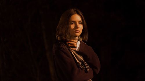Portrait of young woman standing against black background