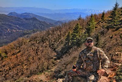 Man wearing camouflage clothing while sitting on rock