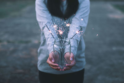 Midsection of woman with illuminated sparklers in jar