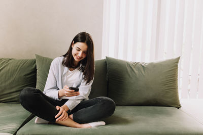 Young woman using mobile phone while sitting on sofa